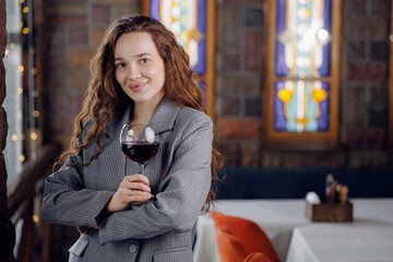 Young caucasian female sommelier holding red wine glass in elegant restaurant setting