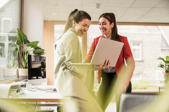 Smiling colleagues standing and using laptop at office