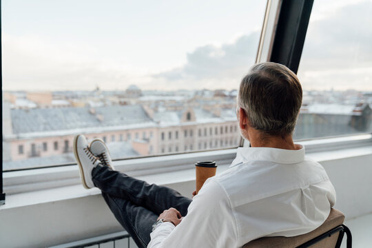 Businessman with disposable coffee cup looking through window in office