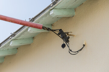 Détail d'un câblage électrique fixé sous un toit en bois dans un environnement résidentiel en plein jour.