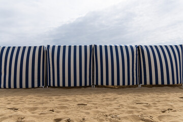 Cabines de plage rayées à marée basse sous un ciel nuageux dans une station balnéaire.