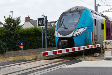 Train moderne circulan près d'un passage à niveau, avec une barrière abaissée à l'entrée de la voie ferrée.