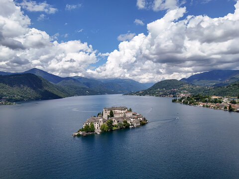 Aerial view of Isola San Giulio, a jewel of stone and history rising from the cerulean waters of Lake Orta, under a sky brushed with clouds, Orta San Giulio, Piedmont, Italy.