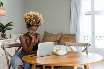 Young African american woman using laptop working at home while having a breakfast. Copy space.