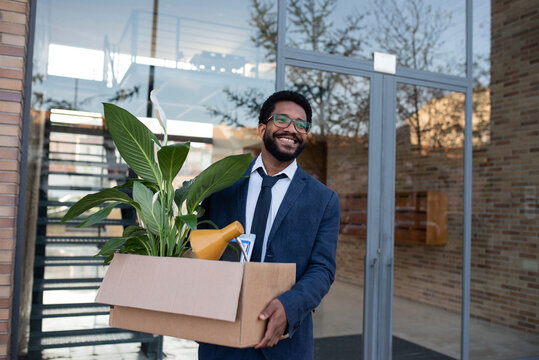 Smiling businessman leaving office building carrying cardboard box