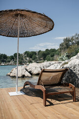 Wooden sunbed and straw beach umbrella on a seaside deck in Turkey, overlooking clear turquoise...
