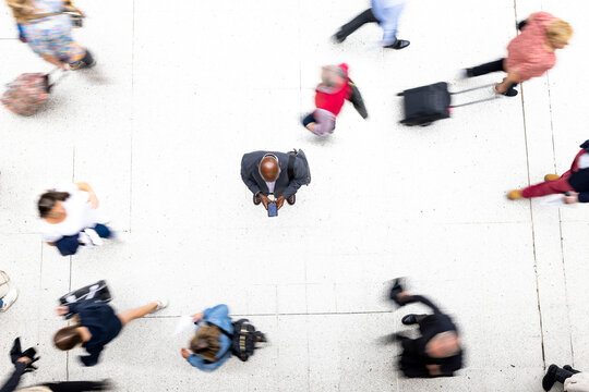 Businessman using mobile phone surrounded by commuters at railroad station