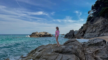 Young woman in a swimsuit on a rocky cliff. Summer beach vibe with scenic seascape and natural textures. Banner for tourism promotion.