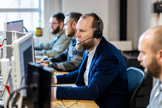 Mature businessman wearing headset sitting at desk with colleagues