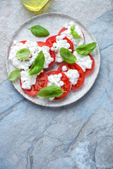 Caprese with cottage cheese, tomatoes and basil, vertical shot on a blue and beige stone...
