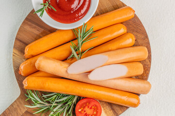 Close-up of uncooked sausages with ketchup, rosemary, and tomato on a wooden cutting board