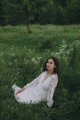 Beautiful model in white dress sits in grass and enjoys nature