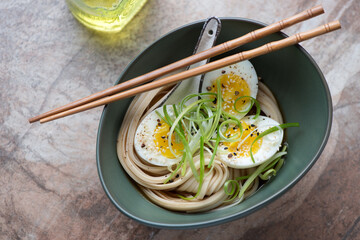 Miso udon with boiled egg served in a green bowl, horizontal shot on a brown granite background,...