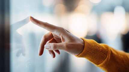 Woman’s hand in a yellow sweater touches a digital touchscreen interface in a modern setting.