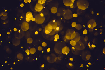 Defocused  golden bokeh lights in various sizes and colors on a dark background creating a dreamy...