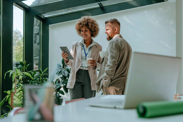 Smiling businesswoman having discussion with businessman over tablet PC in office
