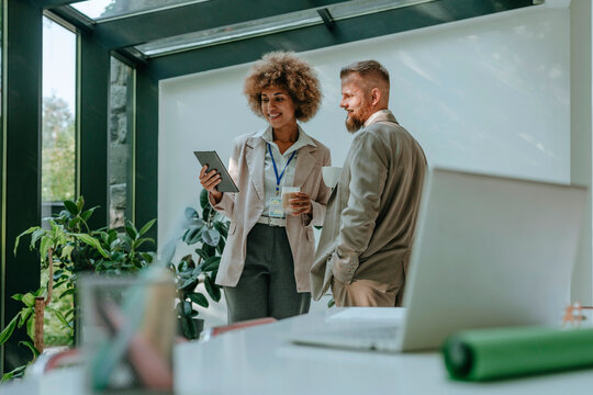Smiling businesswoman having discussion with businessman over tablet PC in office
