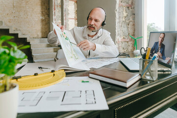 Architect discussing over blueprint with colleague on video call through laptop at desk