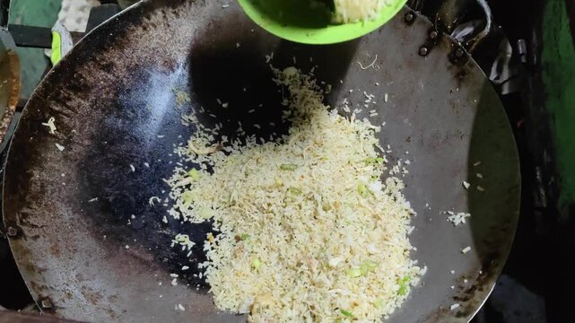A street food vendor skillfully stir-frying Indonesian fried rice (nasi goreng) in a large wok over an open flame. The sizzling sound, smoky aroma, and fast hand movements capture the authentic 