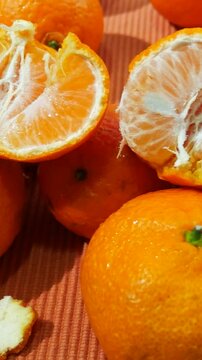 Ripe tangerines are on the table. One of the tangerines is broken in half, orange slices are visible