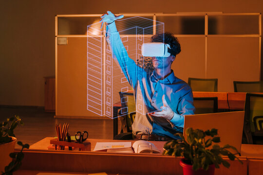 Architect wearing virtual reality simulator and examining blueprint interface in office