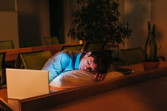 Tired businessman sleeping on pillow at desk in office