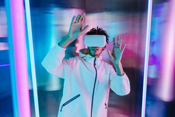 Young man wearing virtual reality headset and gesturing in front of illuminated wall