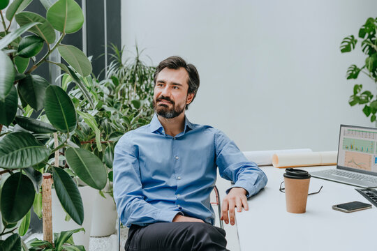 Smiling businessman sitting near plants at desk in office