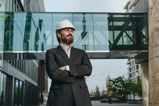 Thoughtful architect with arms crossed standing in front of elevated walkway