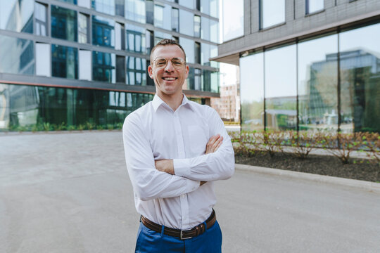 Smiling businessman with arms crossed standing outside office building