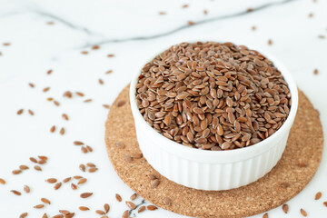 Flax seeds in a bowl isolated on white kitchen table. Close-up.