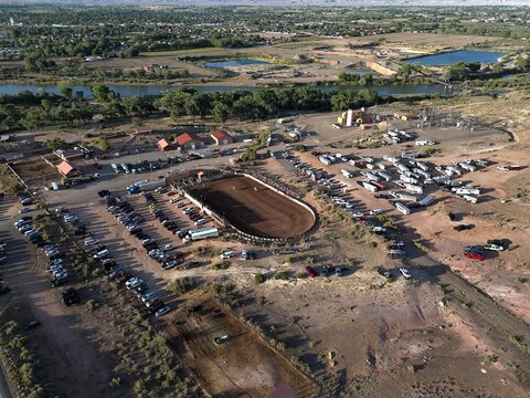 Aerial view of a rodeo arena bathed in golden sunlight, surrounded by parked vehicles and the meandering Colorado River, Fruita, Colorado, United States.