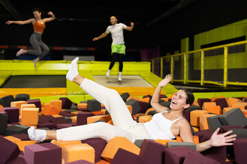 Happy excited young girl playfully diving into colorful foam cube pit at lively indoor trampoline...