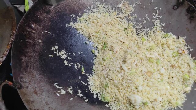 A street food vendor skillfully stir-frying Indonesian fried rice (nasi goreng) in a large wok over an open flame. The sizzling sound, smoky aroma, and fast hand movements capture the authentic 