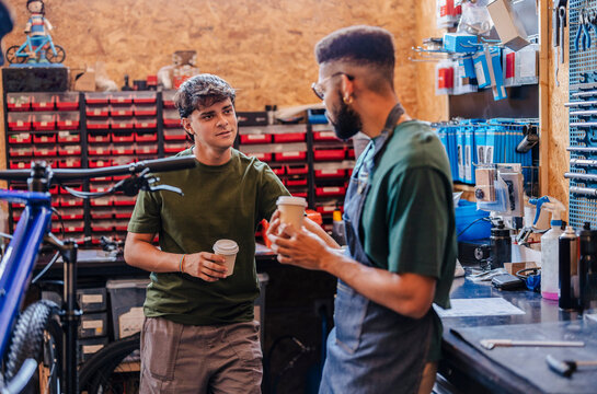 Two men drinking coffee and chatting in bike shop - Powered by Adobe