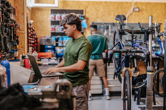 Bicycle mechanic using laptop in busy workshop managing orders