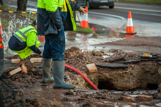 Workers in hi-vis gear standing around a mud hole in the road