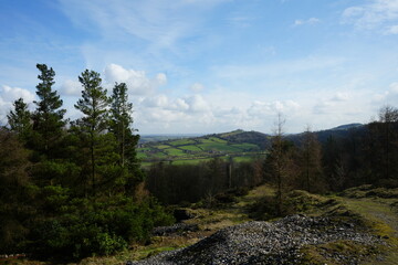 Obraz premium North East Derbyshire, England - March 6 2024: Scenic view of spring patchwork fields and woodland hills under blue sky