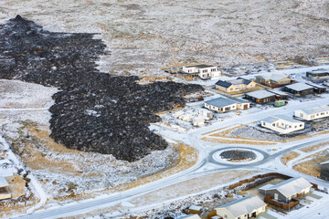 Aerial view of stark black hardened lava flow encroaching on a snow-dusted town, a dramatic contrast of destruction and resilience, Grindavik, GrindavÃ­kurbÃ¦r, Iceland.