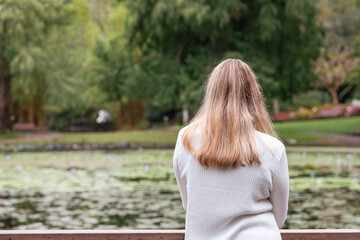 person standing at a wooden railing overlooking a lake with lily pads. The background features trees