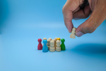 A hand picks a wooden figure from a group of multicolored and neutral wooden pawns, symbolizing leadership, decision-making, recruitment. Ideal for team building, human resources, leadership