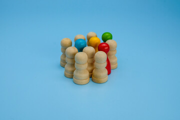 A group of natural wooden pawns tightly surrounding several colorful pawns red, yellow, green, and blue. Symbolizing the concept of diversity, inclusion, or possibly cultural pressure and conformity