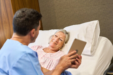 Senior woman in bed with nurse showing her a tablet device