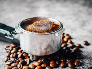 Close-up ground coffee in portafilter and roasted coffee beans or filter coffee handle on gray background