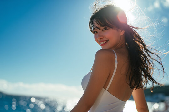 Smiling woman in white dress / white swimsuit by the sea on a sunny day

