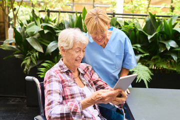 Senior Woman and Caregiver Viewing Tablet in Rehab Facility Garden
