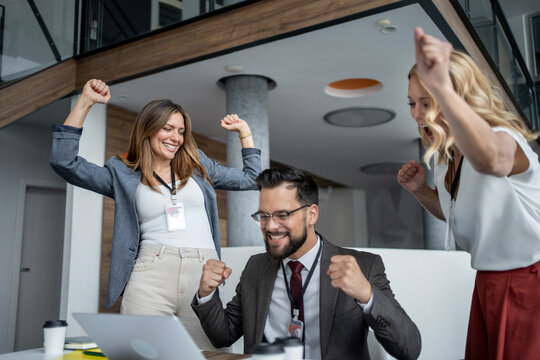 Excited business team celebrating success with laptop in modern office
