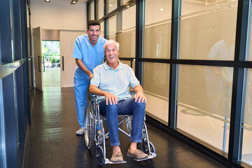 Caregiver assisting senior in wheelchair at modern rehabilitation facility hallway