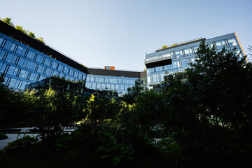 Modern glass office building surrounded by lush greenery under a clear sky