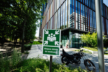 Evacuation assembly point sign near a modern building and motorcycle in Warsaw
